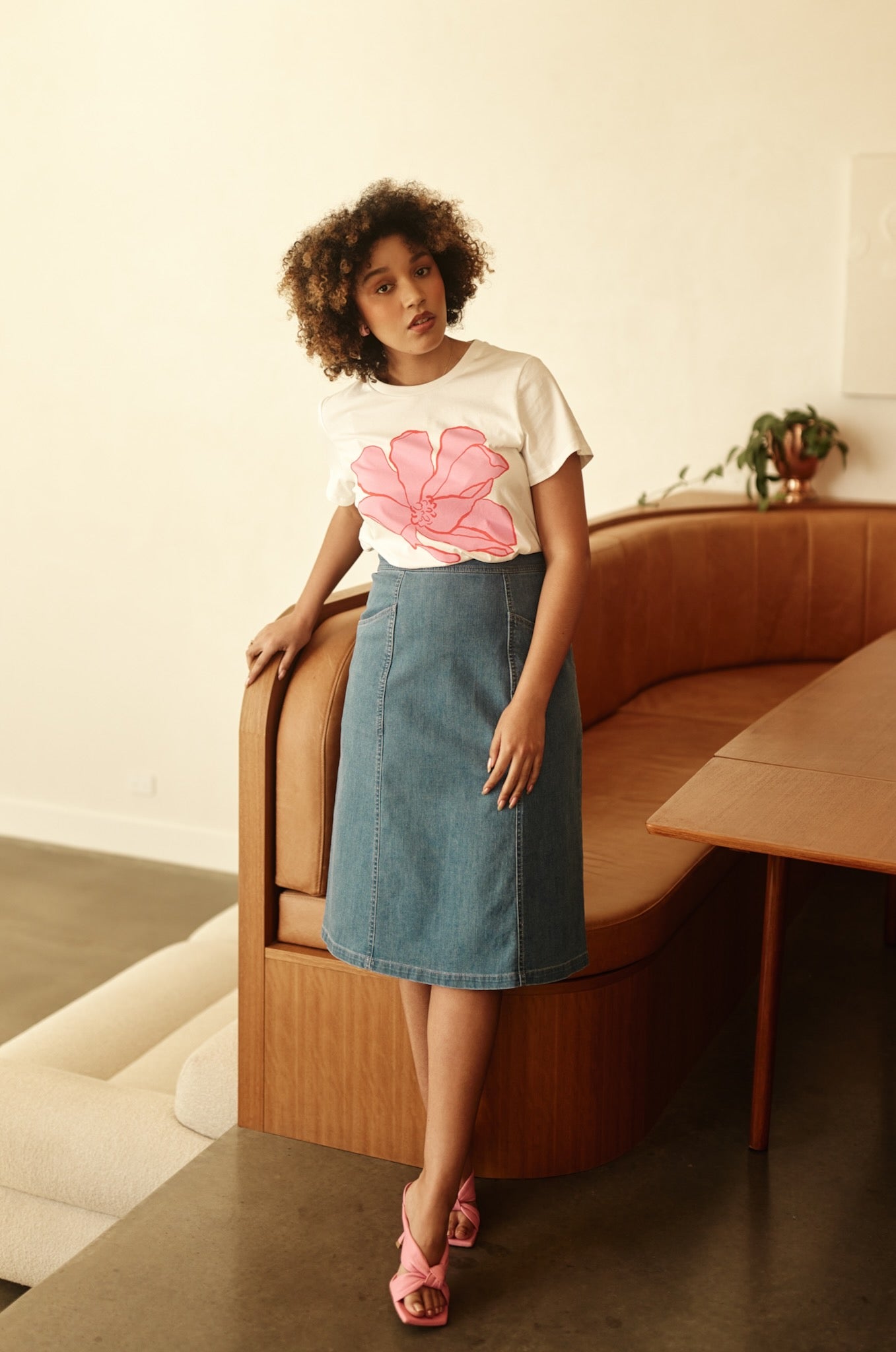 Woman wearing a white t-shirt with a pink flower design and a denim skirt, sitting on a wooden bench.