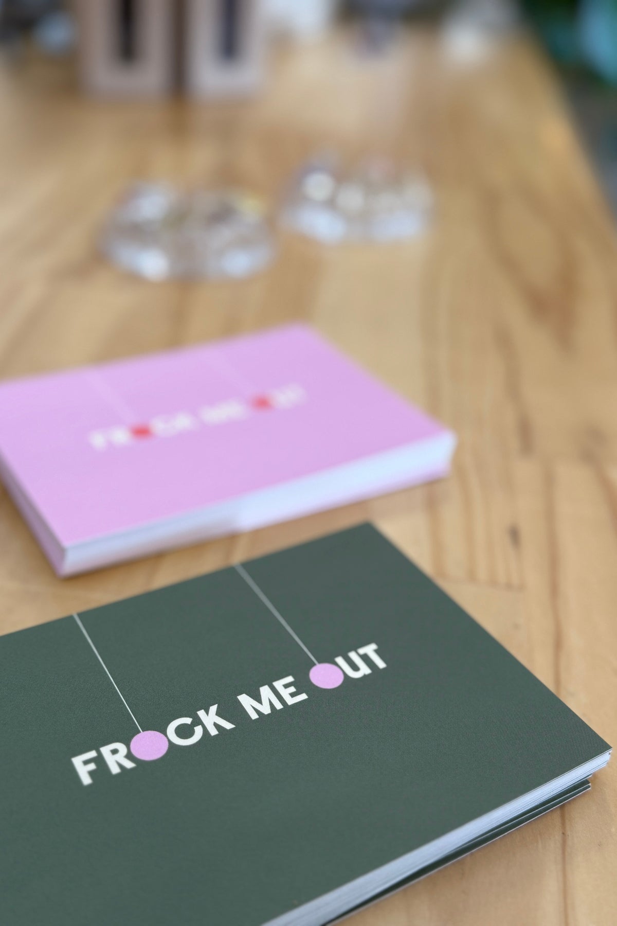 Two vouchers on a wooden surface, one titled 'Frock Me Out' with a pink cover.
