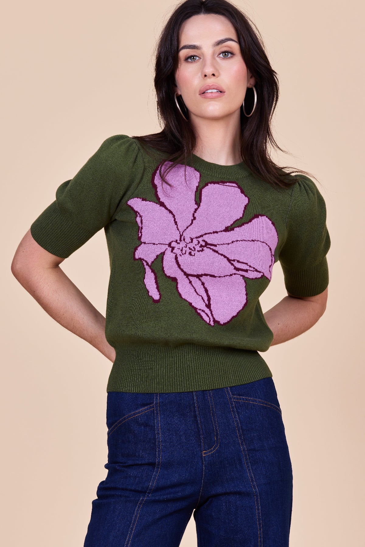 Woman wearing an olive knit top with a lilac floral design on a cream background