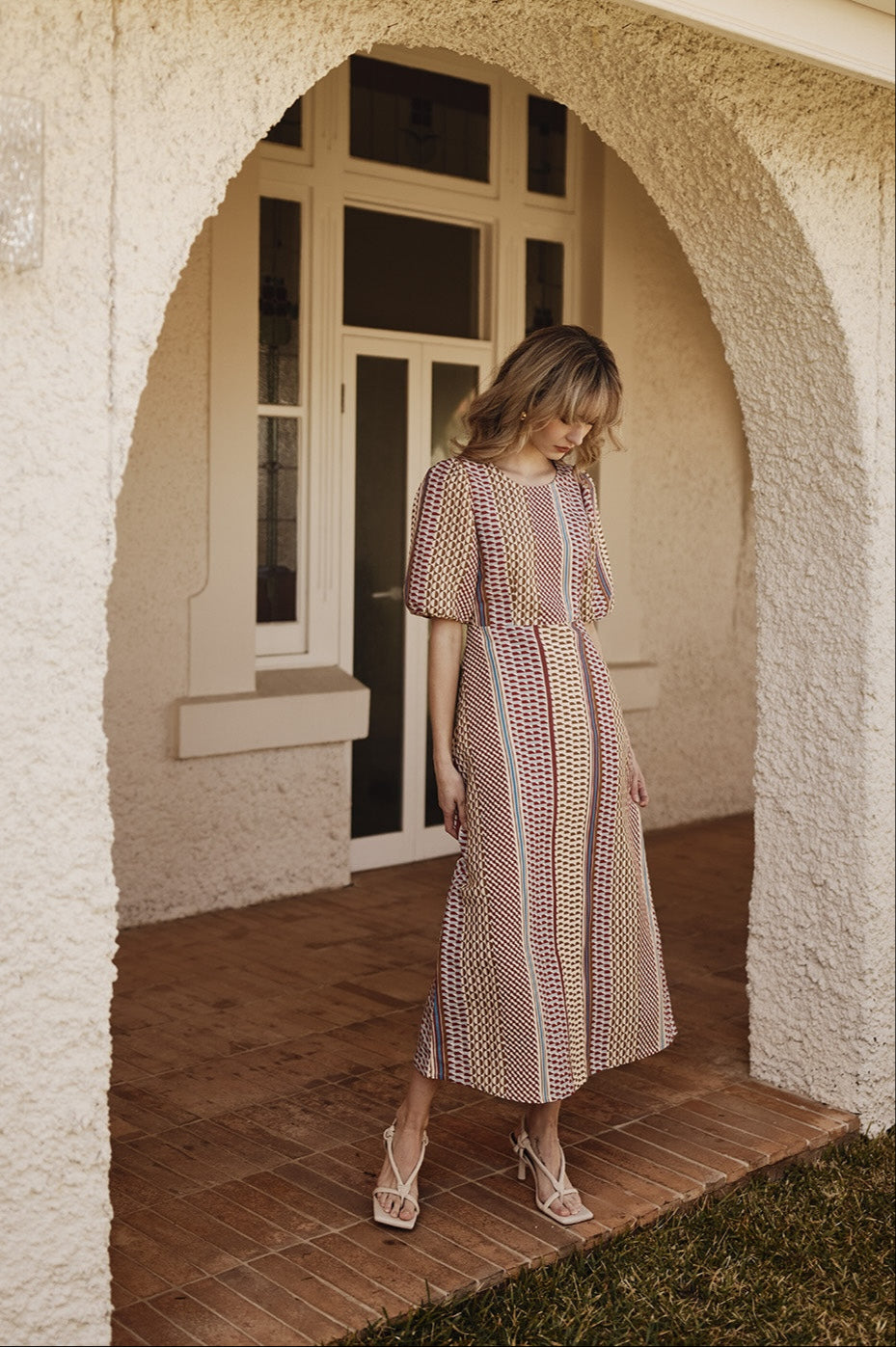 Woman in a patterned dress standing in an archway of a house.